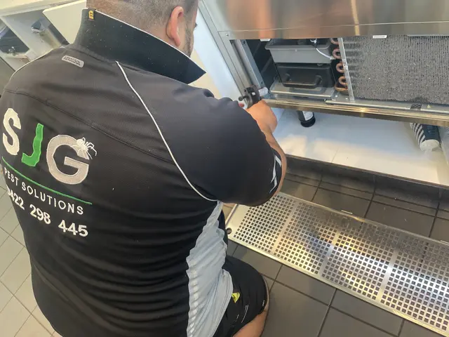 SJG technician servicing pest controls behind commercial kitchen equipment